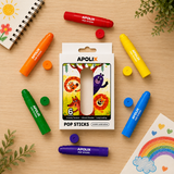 A set of six Apolix Pop Sticks crayons in assorted colors, arranged around their retail packaging on a light wood tabletop. The packaging features cartoon animal illustrations.