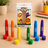 A set of six Apolix Pop Sticks crayons in assorted bright colors, arranged in front of their illustrated white packaging box on a light wood tabletop. The crayons are shown uncapped with their caps placed beside them.