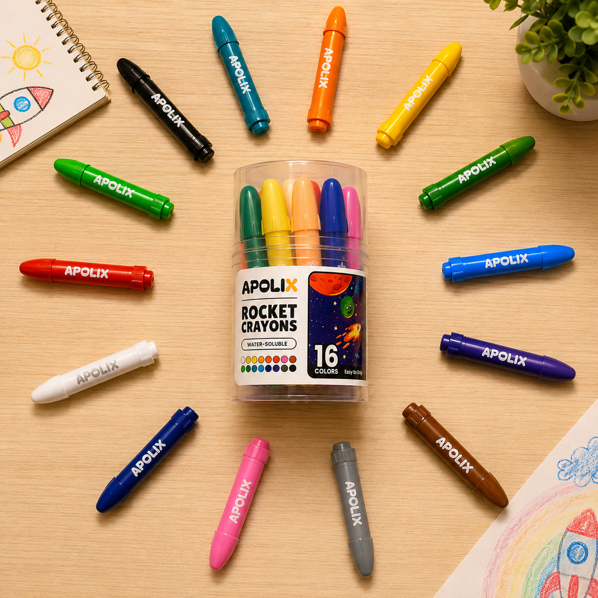 A clear plastic tub of APOLIX Rocket Crayons with 16 colorful crayons arranged in a circle on a light wood desk, surrounded by matching crayons pointing toward the container.