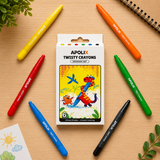 A boxed set of APOLIX Twisty Crayons centered on a light wood surface, surrounded by six colored crayons in yellow, orange, red, green, blue, and black. The package shows colorful cartoon dinosaur artwork and the text 'APOLIX TWISTY CRAYONS' and '6 Twisty Stripes + Smooth Coloring.